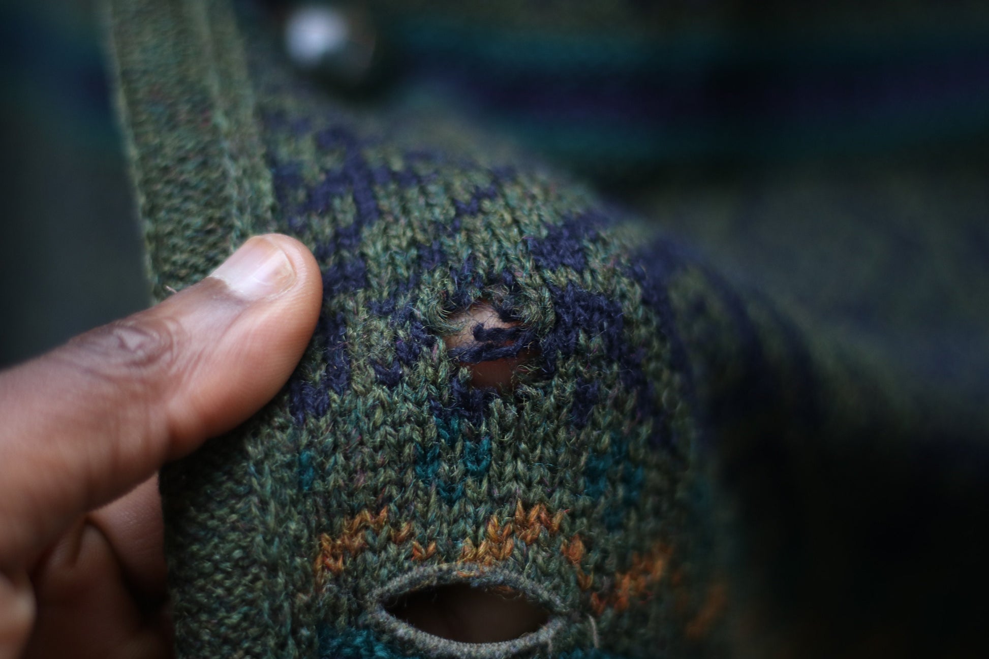 Close up of multi-colored cardigan with green, orange, and purple stripes . Shows small hole in the knit. The long-sleeved vintage design can be worn as a coat and it is perfect for fall and winter fashion.