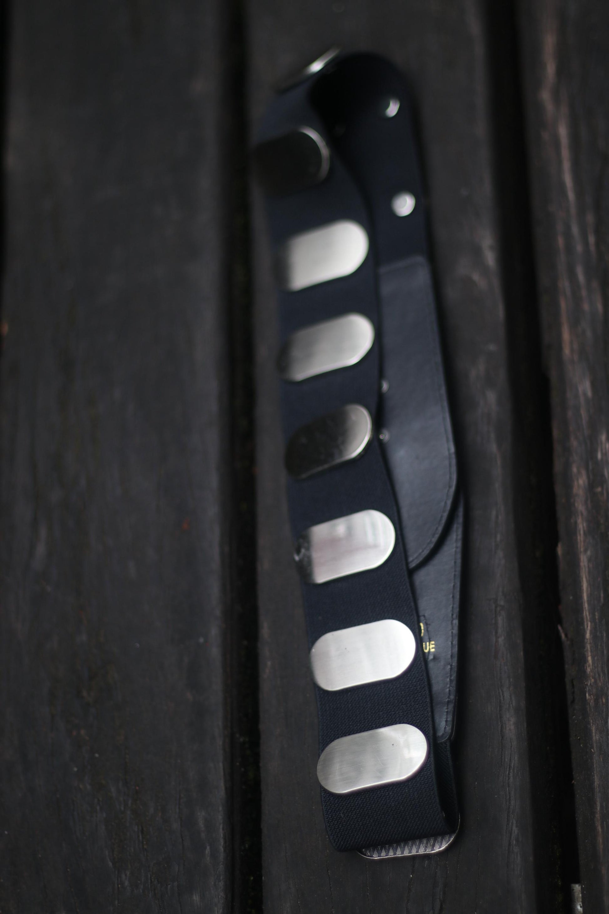 Vintage y2k Black leather belt with metallic silver-toned rivets and a large ring, on a wooden surface.