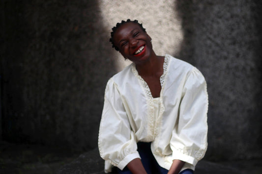 Stylish woman poses smiling, wearing a vintage white blouse with intricate lace detailing. Set against a textured gray background, the image captures elegance and timeless fashion. #Fashion #VintageLook #StylishOutfit #LifestylePhotography