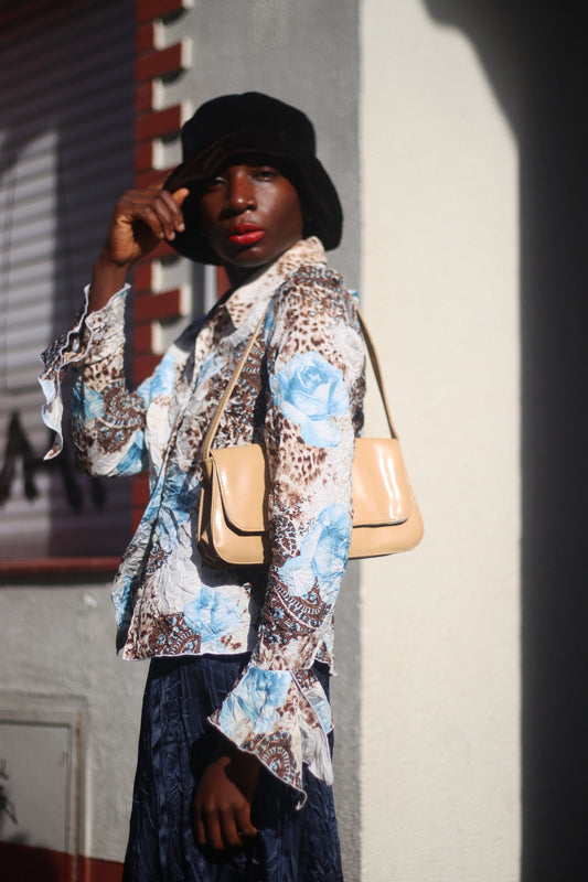 Model of African Heritage in a vintage y2k floral print shirt with butterfly sleeves and dark skirt, carrying a beige shoulder bag standing in sunlight.