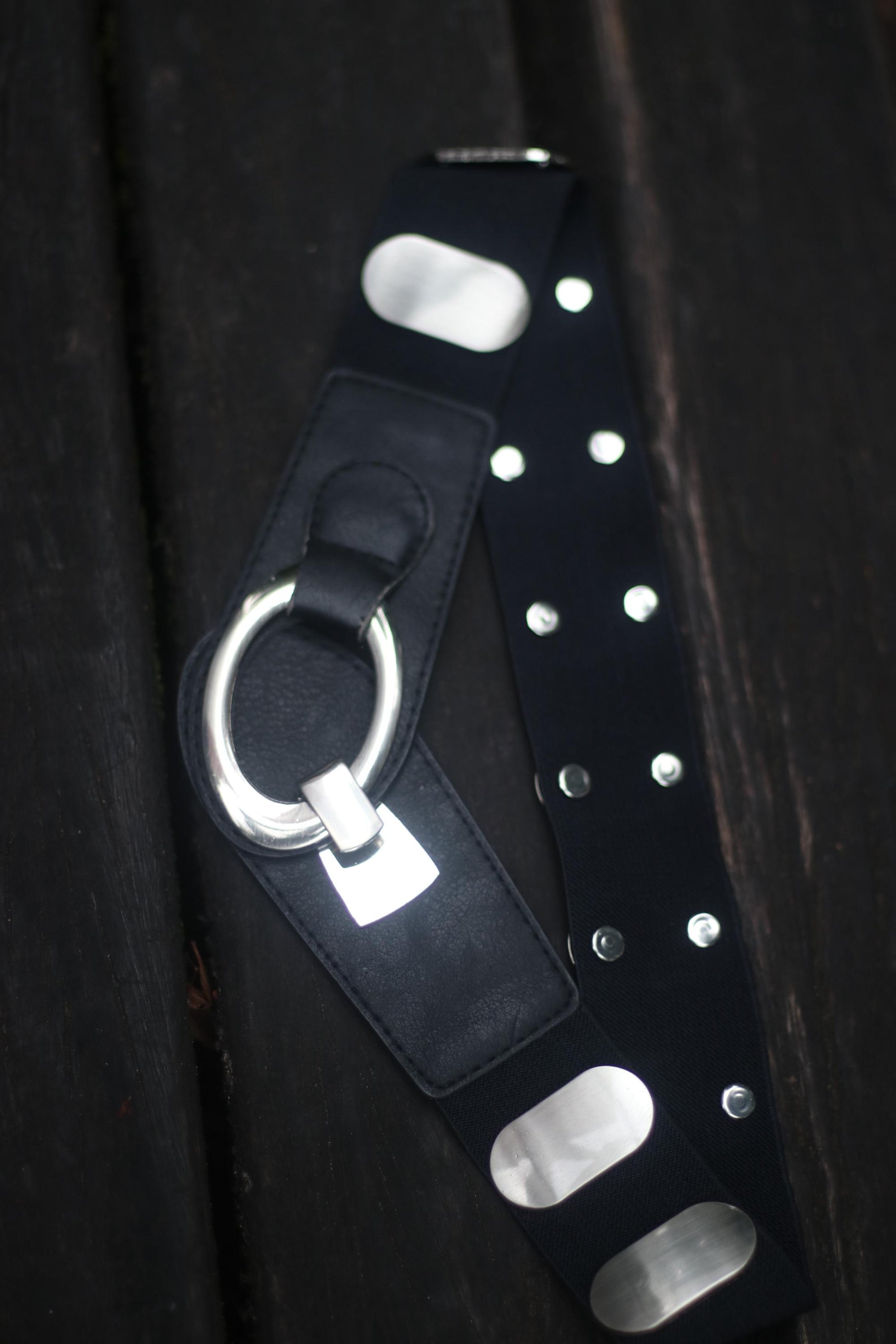 Black leather belt with silver rivets and buckle on a wooden surface.