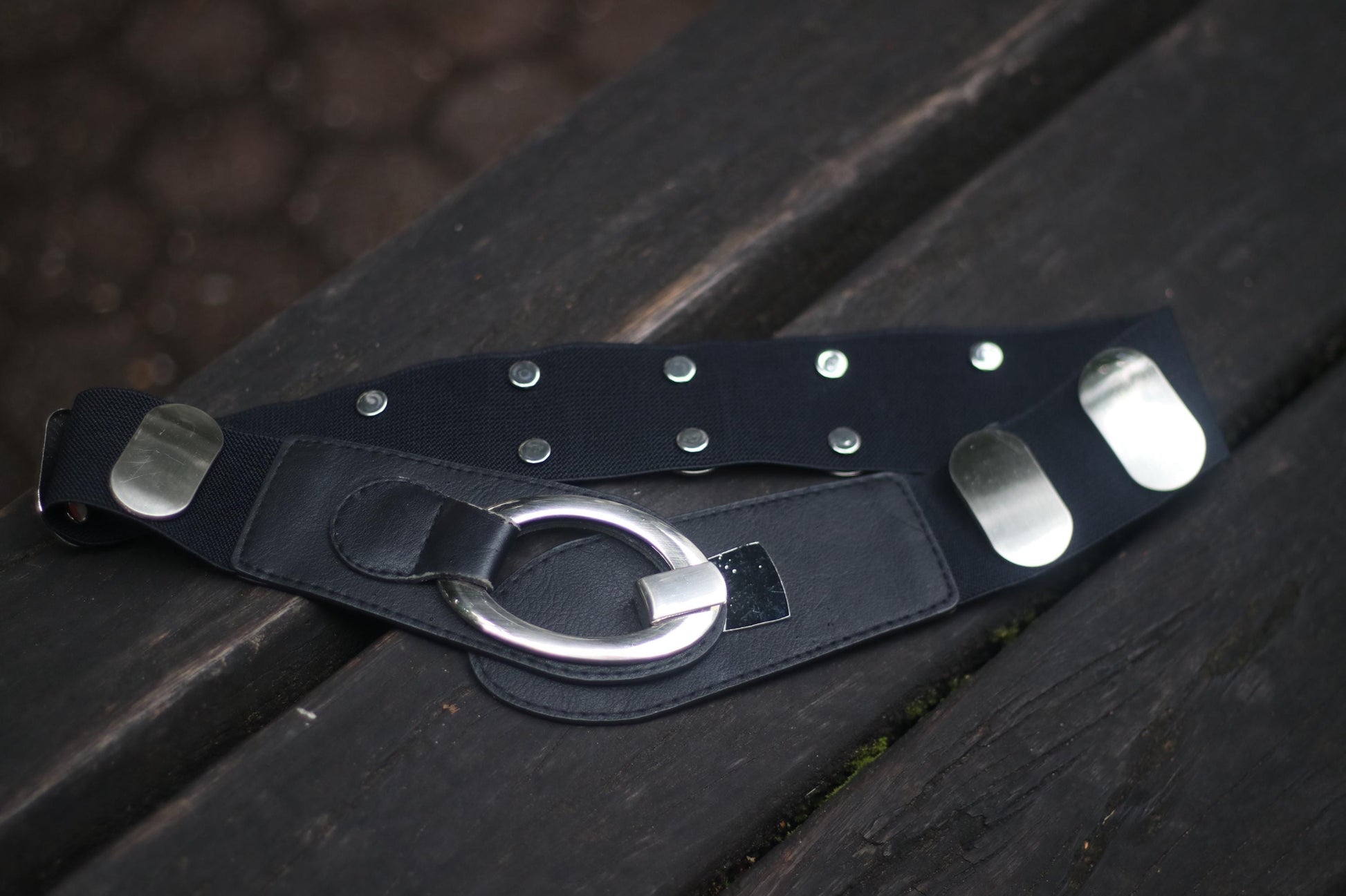 Vintage y2k Black leather belt with metallic rivets and a large ring, on a wooden surface.