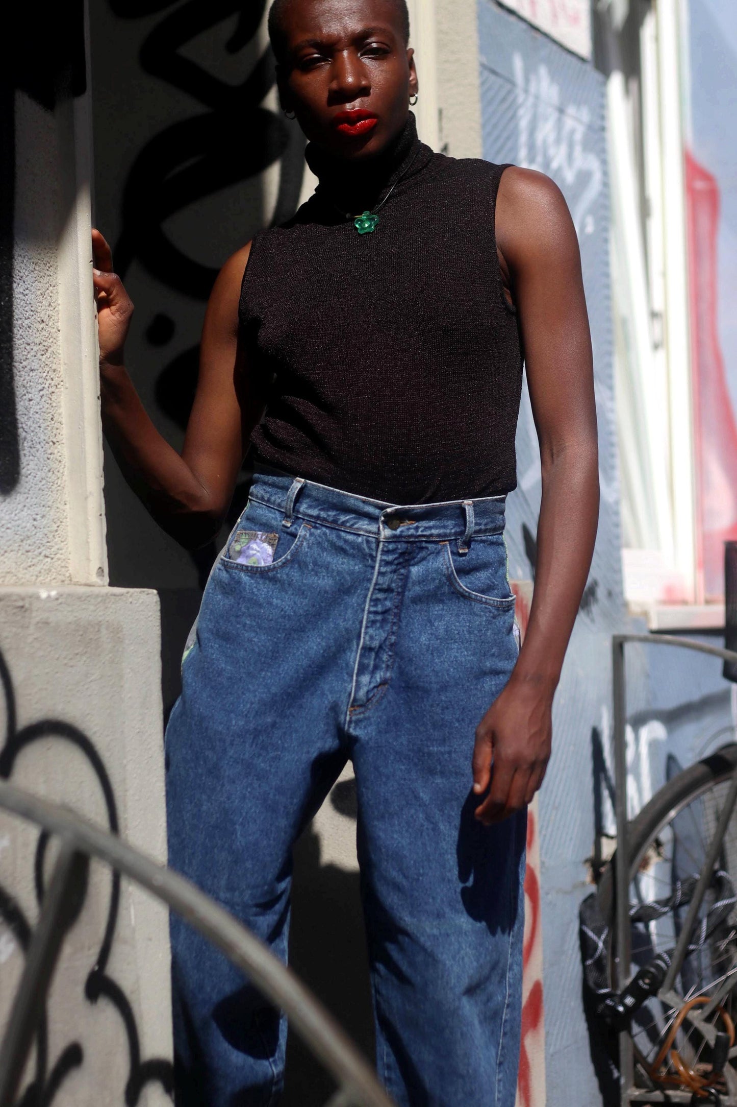 A black women in vintage high-waisted jeans from the 80s and a black sleeveless top photographed against an urban background. The jeans have floral patchwork side details