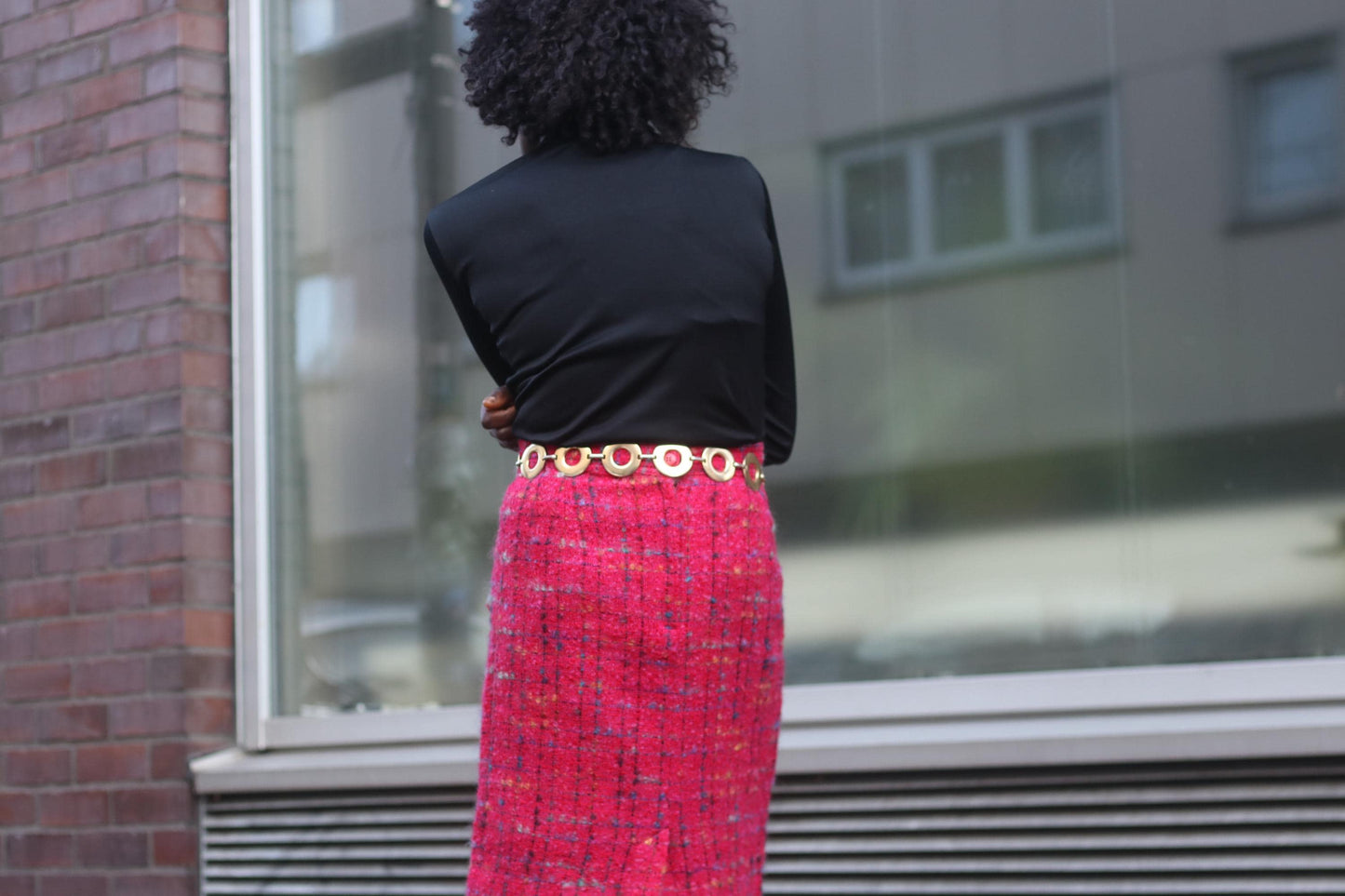 Fashionable woman in a pink boucle like skirt , turtleneck and belt photographed from the back, without her face showing. She wears a