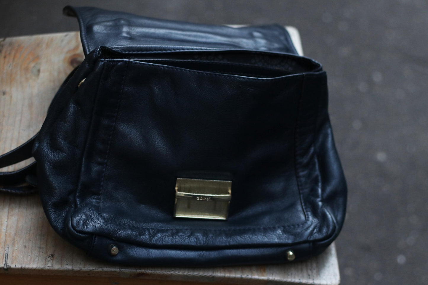 Close-up of an open, vintage black leather shoulder bag on a weathered wooden surface.  Focus on the silver-toned clasp and the texture of the aged leather.  The bag&#39;s interior is visible, showcasing its spaciousness.