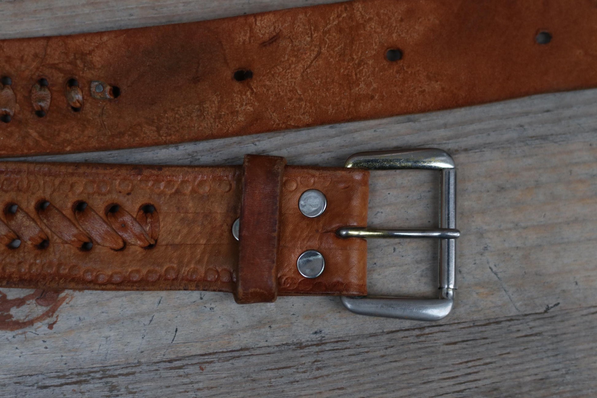 Close-up of a vintage Western brown leather belt, emphasizing the detailed handwoven texture and classic  silver toned cowboy buckle. The unisex 70s  belt is placed on a rustic wooden chair highlighting its craftsmanship and Cowgirl  heritage.