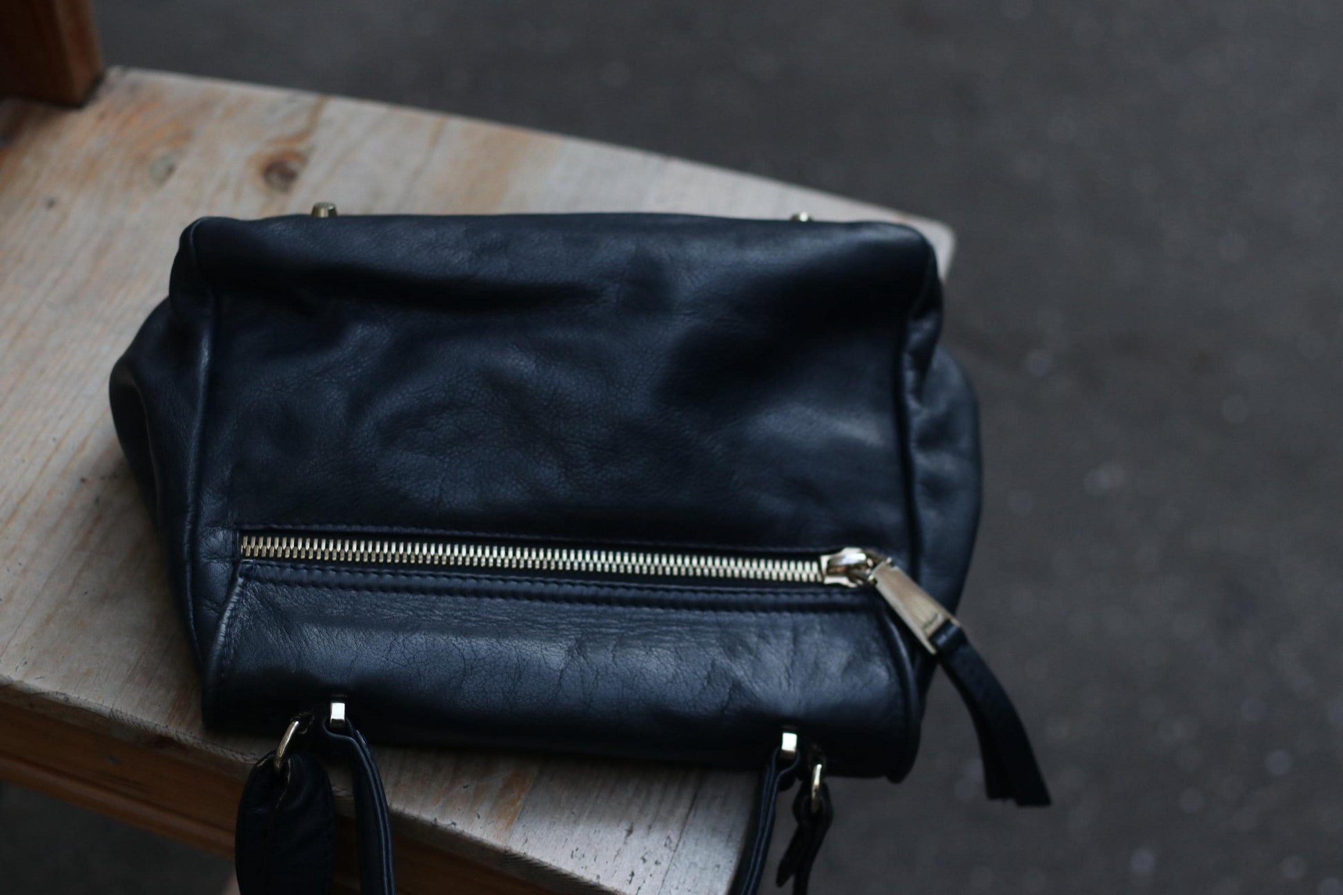 A vintage Black leather top-handle and shoulder bag from the 90s by the brand Abro is captured on wooden surface.  the image focuses on the back compartment with a silver-toned zipper