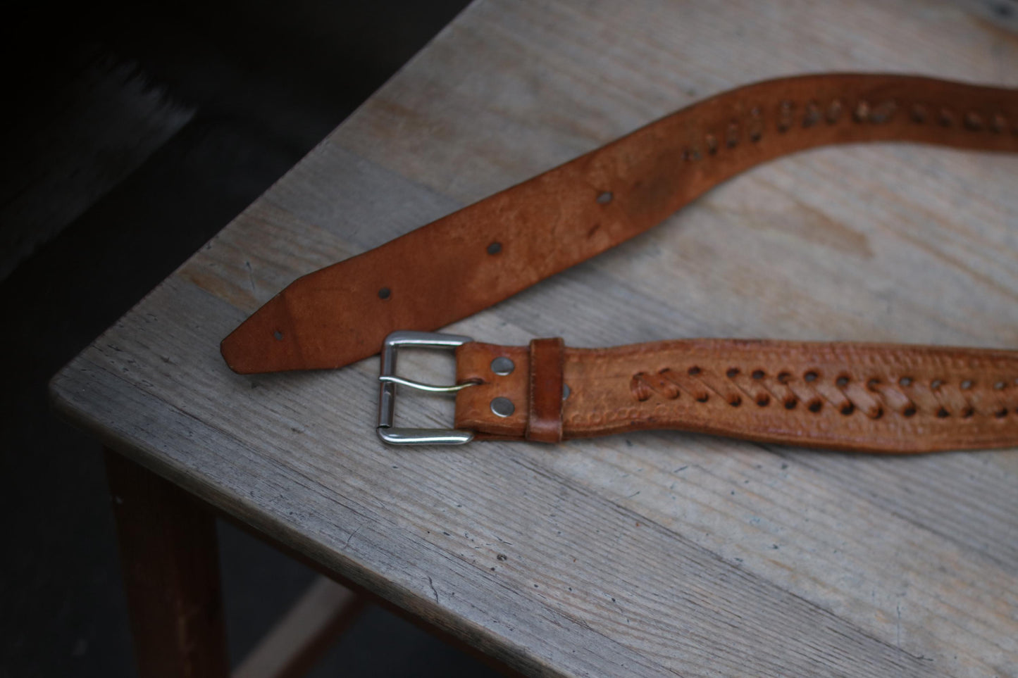 A photograph of a vintage Western woven leather belt on a wooden chair. The image highlightes the beautiful handwoven texture, craftsmanship, and classic silver-toned cowboy buckle.