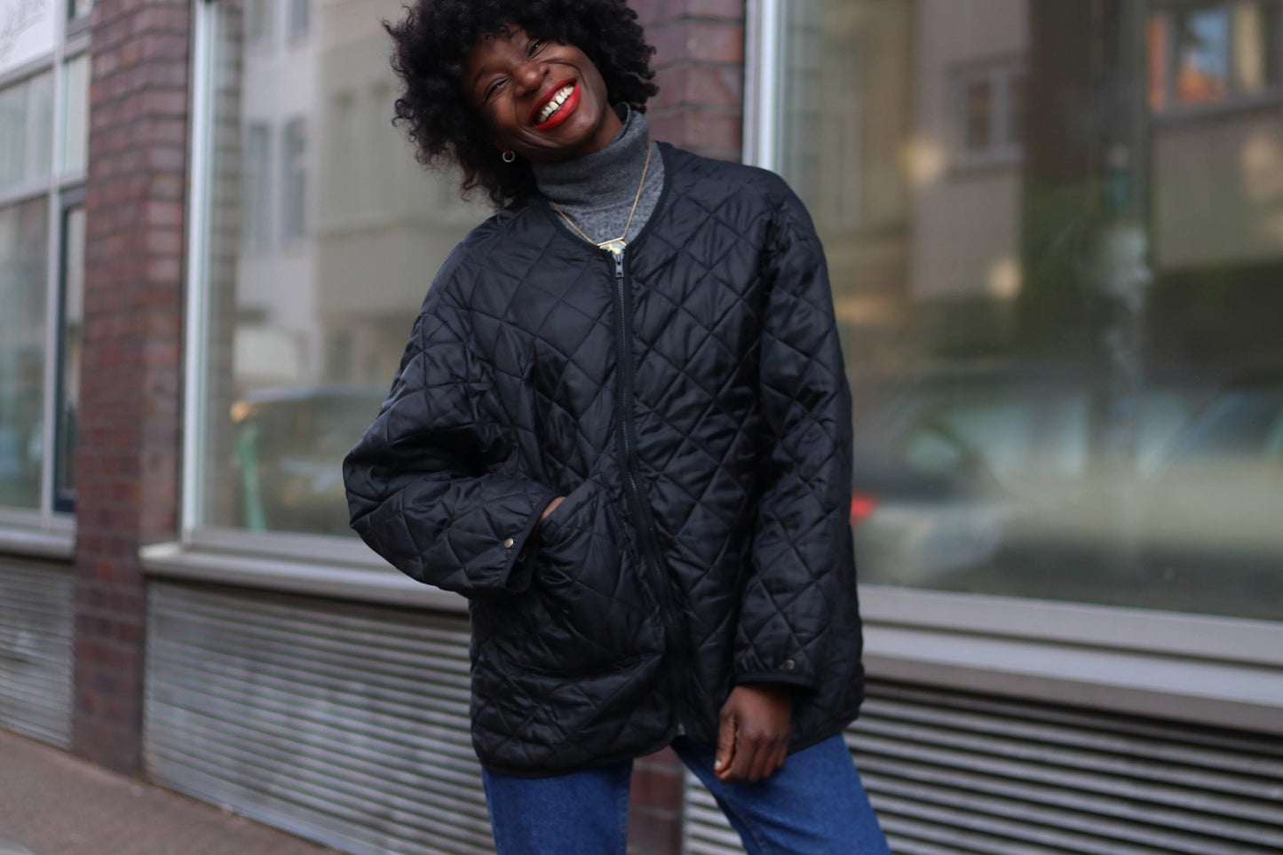 A stylish y2k black quilted vintage jacket with an oversized fit, worn by a smiling woman on the street.